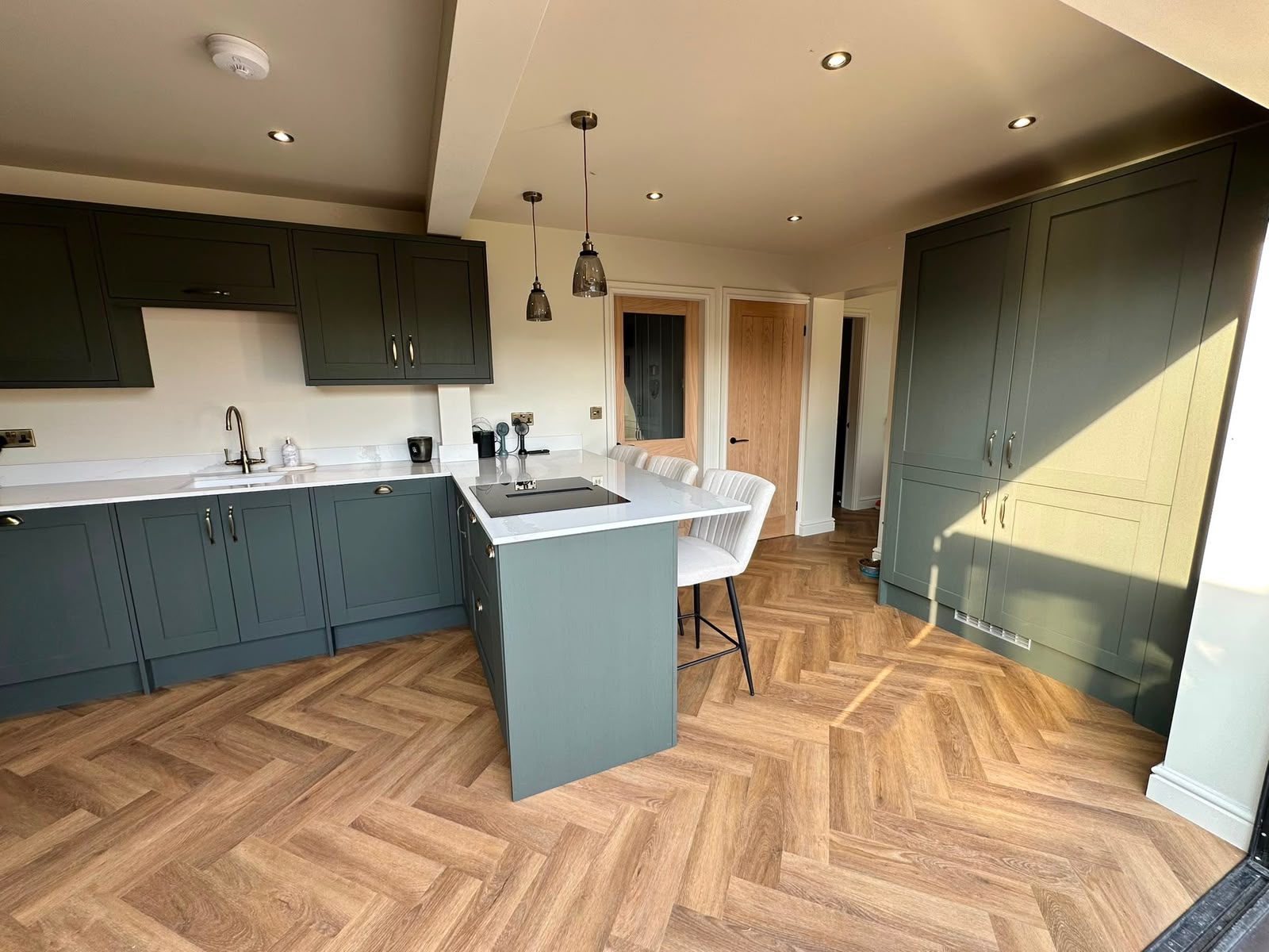 Green shaker kitchen peninsula with a quartz breakfast bar and brass pendant lights
