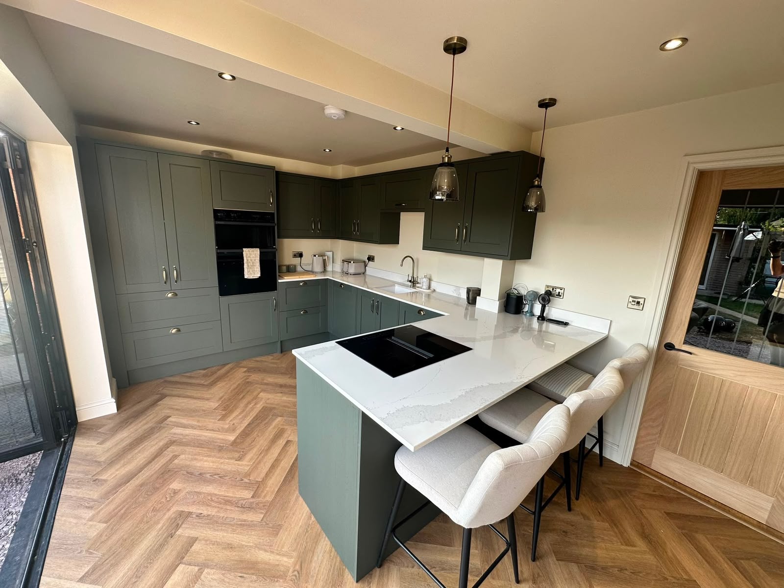 Fitted shaker kitchen in deep green with quartz worktops and herringbone flooring